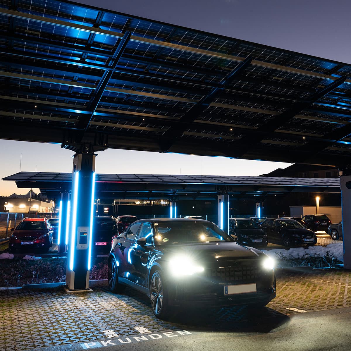 Stilvolle Ladestationen mit LED-Beleuchtung bei Nacht Elektrofahrzeuge unter beleuchtetem Solarcarport in der Nacht