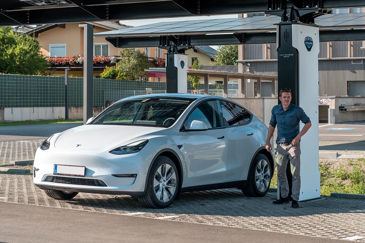 E-Mobilität trifft auf Solarenergie – Ladepark mit PV-Carport Mann steht neben Tesla unter einem Solarcarport mit Ladesäule