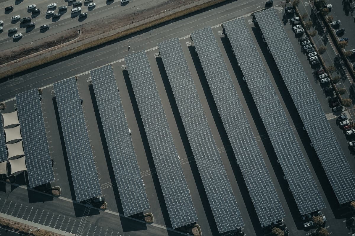 Luftaufnahme von Solar-Carports auf großer Parkplatzfläch Mehrere Reihen von mit Photovoltaik überdachten Stellplätzen auf einem großen Parkplatz an einer Straße