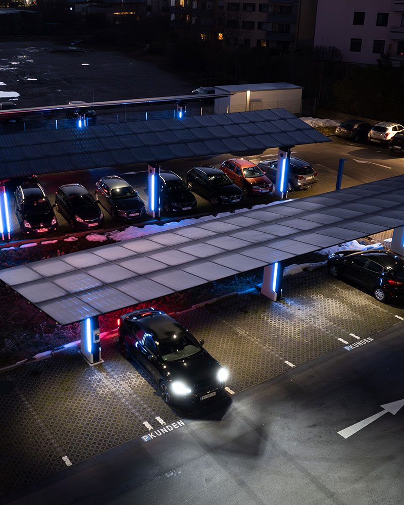 PV-überdachte Kundenparkplätze bei Nacht Kundenparkplätze unter beleuchtetem Solarcarport mit E-Auto bei Nacht
